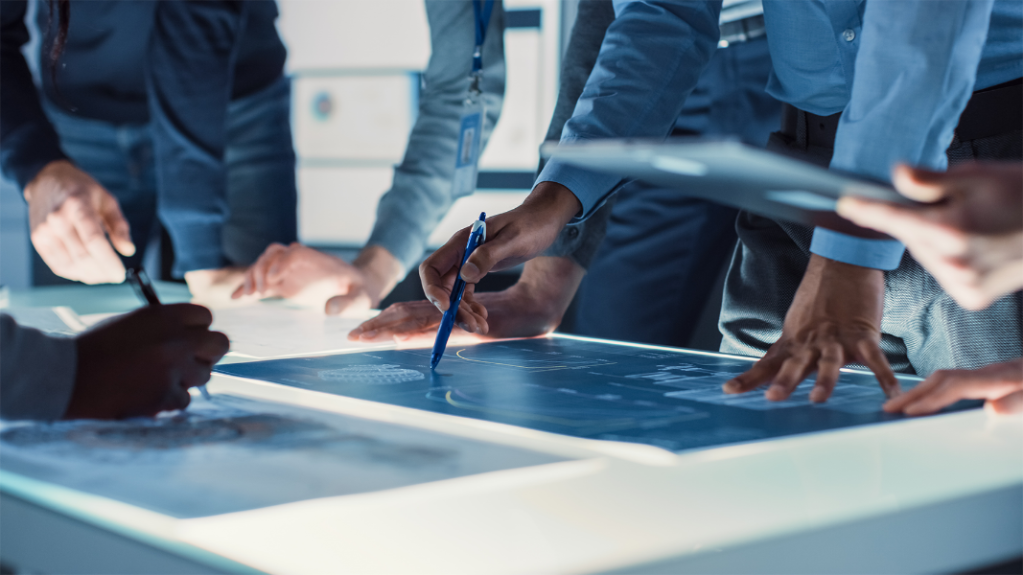 Multiple people standing over a blueprint with the main subject holding a pencil
